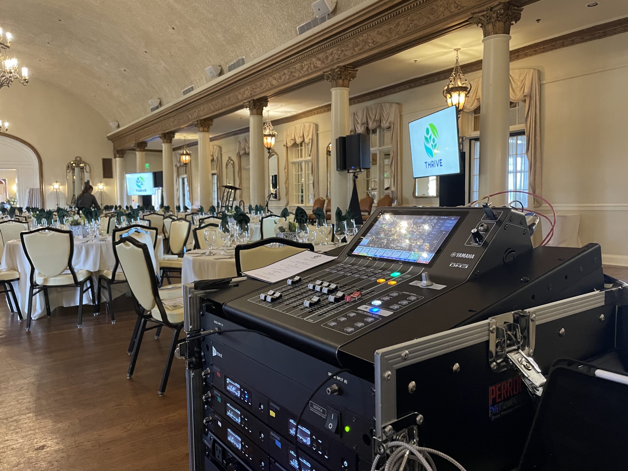 A sound system setup near the neatly arranged white tables, chairs, glassware, and a screen showing the THRIVE logo.