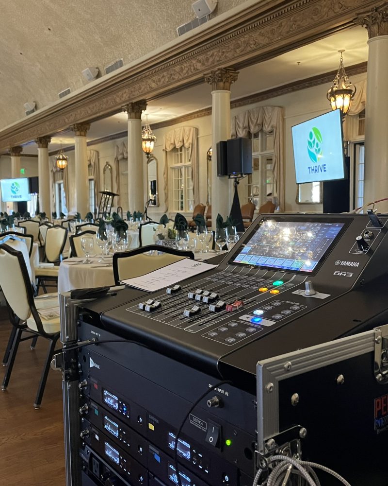 A sound system setup near the neatly arranged white tables, chairs, glassware, and a screen showing the THRIVE logo.